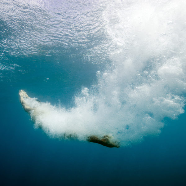 Diving into the sea, underwater view looking up to water surface, backlit.